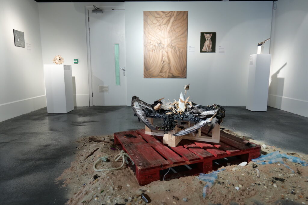 Installation view with a charred form on a red pallet at the centre of the gallery