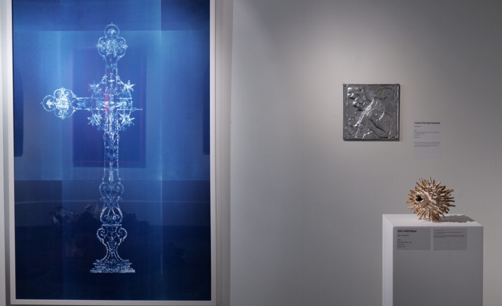Cyanotype crucifix work beside a metal relief and a ceramic sculpture