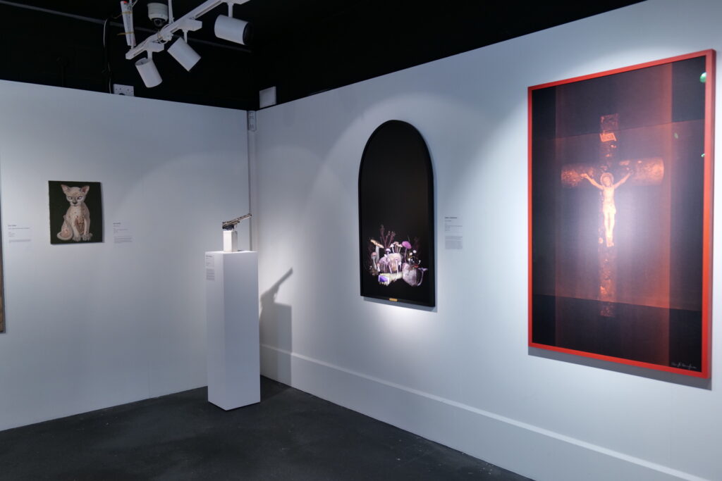 Installation view with a plinth, an arch-framed work and a red-framed crucifix