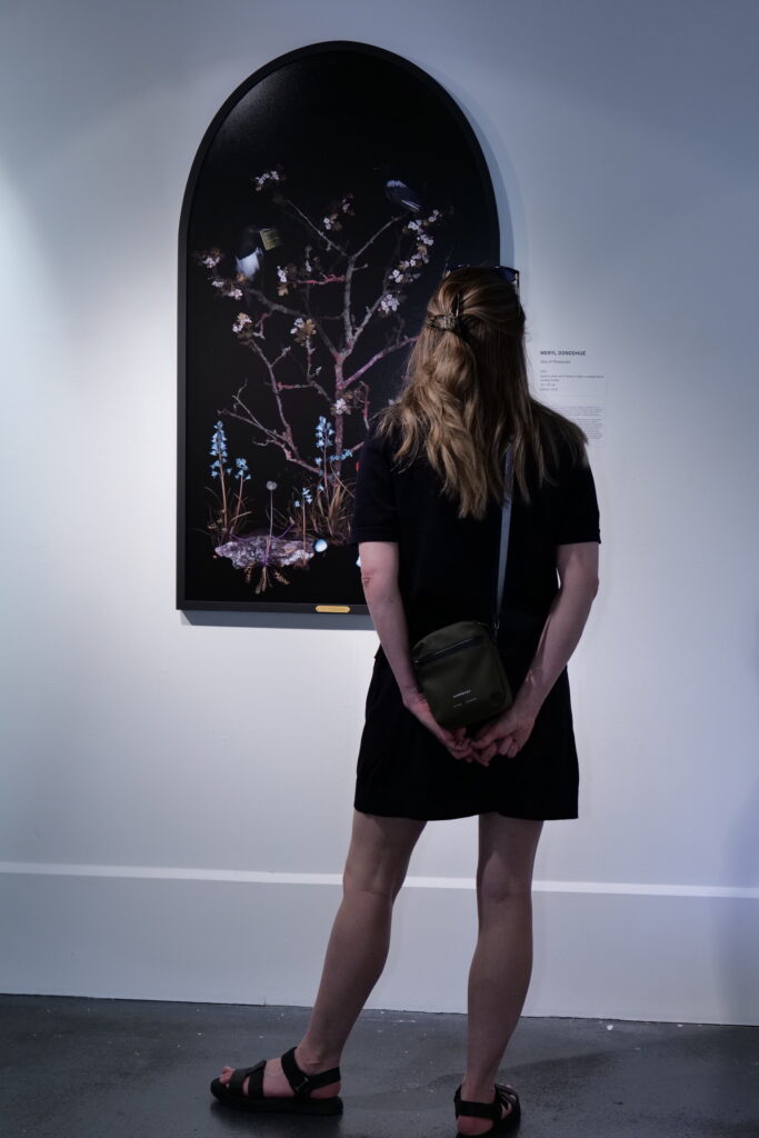 A visitor standing before an arch-framed work of dark botanical forms